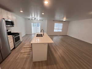 Kitchen featuring appliances with stainless steel finishes, a center island with sink, open floor plan, white cabinetry, and a textured ceiling