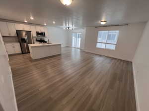 Kitchen featuring open floor plan, white cabinets, appliances with stainless steel finishes, light countertops, and a kitchen island with sink