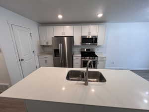 Kitchen with stainless steel appliances, light stone countertops, white cabinetry, recessed lighting, and dark wood finished floors