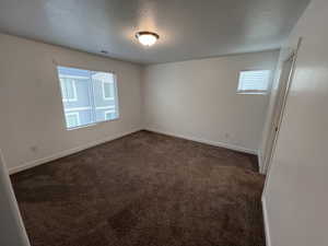 Unfurnished room featuring a textured ceiling and dark colored carpet