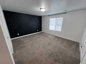 Carpeted empty room with an accent wall, a textured ceiling, and a decorative wall