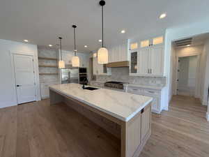 Kitchen featuring open shelves, white cabinets, an island with sink, appliances with stainless steel finishes, and light wood finished floors