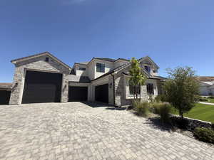 View of front of home featuring decorative driveway, stone siding, an attached garage, and stucco siding