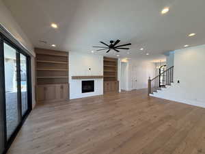 Unfurnished living room featuring built in shelves, light wood-type flooring, stairs, a brick fireplace, and recessed lighting
