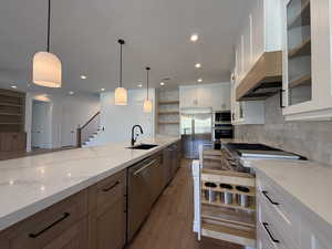 Kitchen featuring open shelves, light wood-style flooring, built in appliances, light stone countertops, and tasteful backsplash