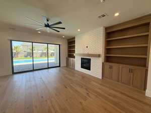 Unfurnished living room featuring built in shelves, ceiling fan, light wood-style flooring, a brick fireplace, and recessed lighting