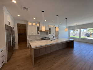 Kitchen with wood finished floors, recessed lighting, paneled built in refrigerator, and white cabinetry