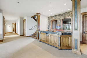 Indoor dry bar with light carpet, decorative columns, recessed lighting, and stairway