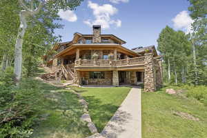 Rear view of house with stone siding, a wooden deck, a yard, a patio area, and a chimney