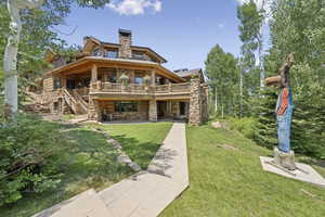 Back of house with stone siding, a yard, a wooden deck, a patio, and a chimney