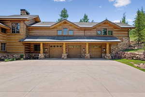 Log-style house featuring stone siding, a garage, concrete driveway, and a chimney
