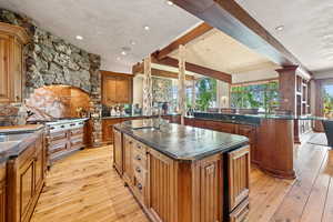 Kitchen featuring an island with sink, light wood-type flooring, beam ceiling, brown cabinetry, and recessed lighting