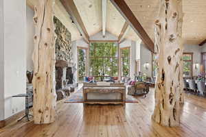 Living room with hardwood / wood-style floors, a stone fireplace, a wooden ceiling with exposed beams, and high vaulted ceiling