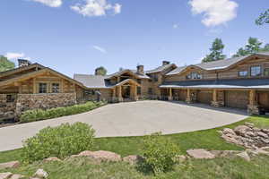 Log cabin featuring stone siding, a chimney, driveway, and a garage