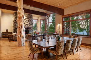 Dining room featuring wood-type flooring, a stone fireplace, and a wood ceiling with exposed beams
