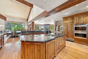 Kitchen featuring beam ceiling, a spacious island, light wood-style floors, stainless steel double oven, and brown cabinets