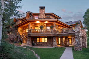 Back of house at dusk featuring stone siding, a patio area, a lawn, stairway, and a chimney