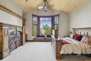 Carpeted bedroom featuring wood ceiling, a fireplace, vaulted ceiling, and a ceiling fan