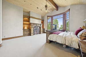 Carpeted bedroom featuring a fireplace, a wood ceiling with exposed beams, and high vaulted ceiling