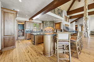 Kitchen featuring beamed ceiling, a kitchen island with sink, high vaulted ceiling, light wood-type flooring, and a kitchen breakfast bar