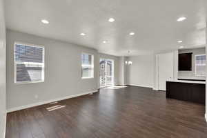 Unfurnished living room featuring a chandelier, a textured ceiling, dark wood finished floors, and recessed lighting