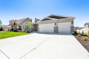 Craftsman-style house with an attached garage, concrete driveway, stone siding, board and batten siding, and a front yard