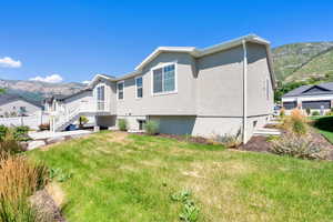 Rear view of house featuring a mountain view, stucco siding, a yard, and a residential view