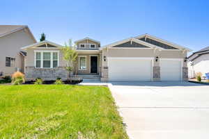 Craftsman-style home featuring stone siding, a garage, a front lawn, concrete driveway, and board and batten siding