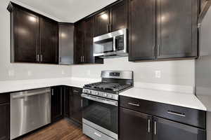 Kitchen featuring stainless steel appliances, dark wood-style flooring, light countertops, dark brown cabinetry, and a textured ceiling