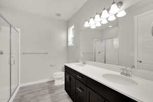 Full bathroom with a stall shower, double vanity, and wood finished floors