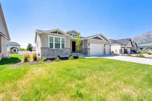 Craftsman house featuring stone siding, stucco siding, an attached garage, driveway, and a front yard