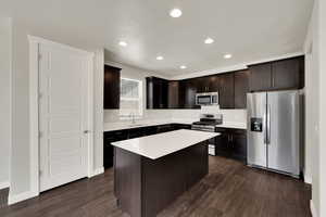 Kitchen featuring appliances with stainless steel finishes, light countertops, dark brown cabinets, dark wood-type flooring, and recessed lighting