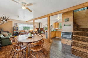 Dining space featuring a wood stove, a textured ceiling, dark wood finished floors, heating unit, and a ceiling fan