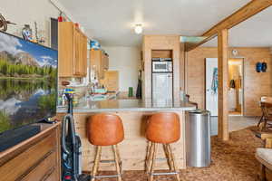 Kitchen with a peninsula, a kitchen breakfast bar, fridge, wood walls, and a textured ceiling