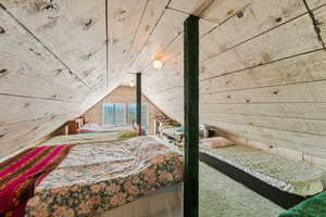 Bedroom featuring wooden walls, vaulted ceiling, and carpet flooring