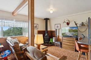 Carpeted living room with a textured ceiling, a wood stove, wooden walls, and beam ceiling