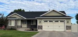 Craftsman-style house featuring stone siding, a garage, driveway, a shingled roof, and a front yard