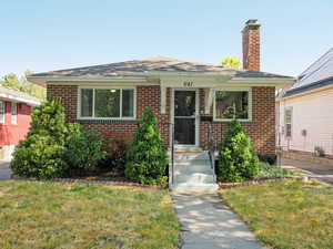 View of front of property featuring brick siding, a chimney, a front lawn, and a shingled roof