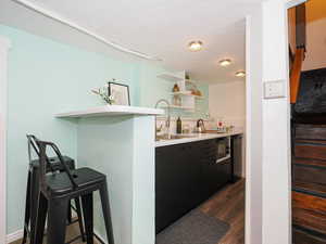 Kitchen featuring dark wood finished floors, open shelves, light countertops, a breakfast bar, and black microwave