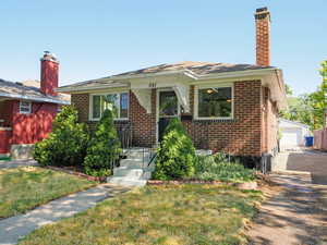 View of front of home with brick siding, a chimney, a front yard, an outdoor structure, and a detached garage