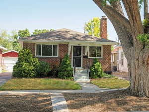 View of front of house with brick siding, roof with shingles, a chimney, and an outbuilding