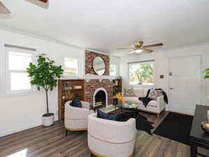 Living area featuring ceiling fan, ornamental molding, dark wood finished floors, a textured ceiling, and a brick fireplace