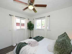 Bedroom with a textured ceiling, multiple windows, wood finished floors, and ceiling fan