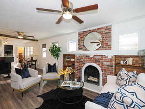 Living room featuring ceiling fan, ornamental molding, a textured ceiling, wood finished floors, and a brick fireplace