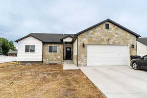 View of front facade featuring an attached garage, stone siding, and driveway