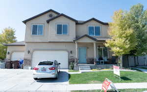 View of front of house featuring a porch, stone siding, concrete driveway, stucco siding, and a front yard