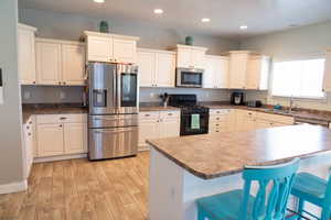 Kitchen featuring stainless steel appliances, a kitchen breakfast bar, light wood-style floors, recessed lighting, and white cabinetry