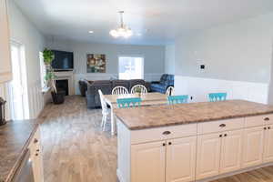 Kitchen with white cabinets, a fireplace, light wood-type flooring, open floor plan, and a wainscoted wall