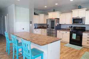 Kitchen featuring appliances with stainless steel finishes, a breakfast bar, light wood-style floors, recessed lighting, and dark countertops