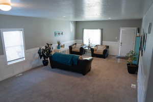 Living room featuring a decorative wall, wainscoting, a textured ceiling, and carpet